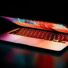 Otwarty laptop z kolorowym podświetleniem klawiatury i ekranu na ciemnym tle.